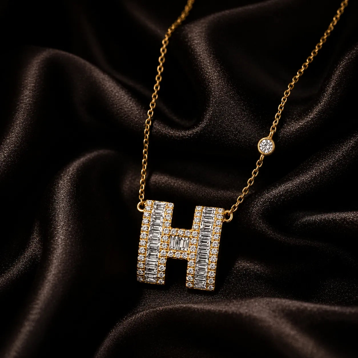 Gold diamond H pendant necklace on a model, featuring luxury jewelry design on black attire.