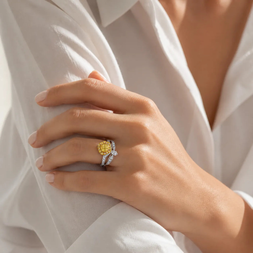 Hand wearing luxury yellow diamond engagement ring, featuring cushion-cut yellow center and white diamond halo, styled on neutral background