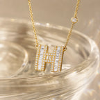 MUHUANG gold "H" pendant necklace with diamonds placed on a transparent surface, emphasizing shimmer and elegant design.