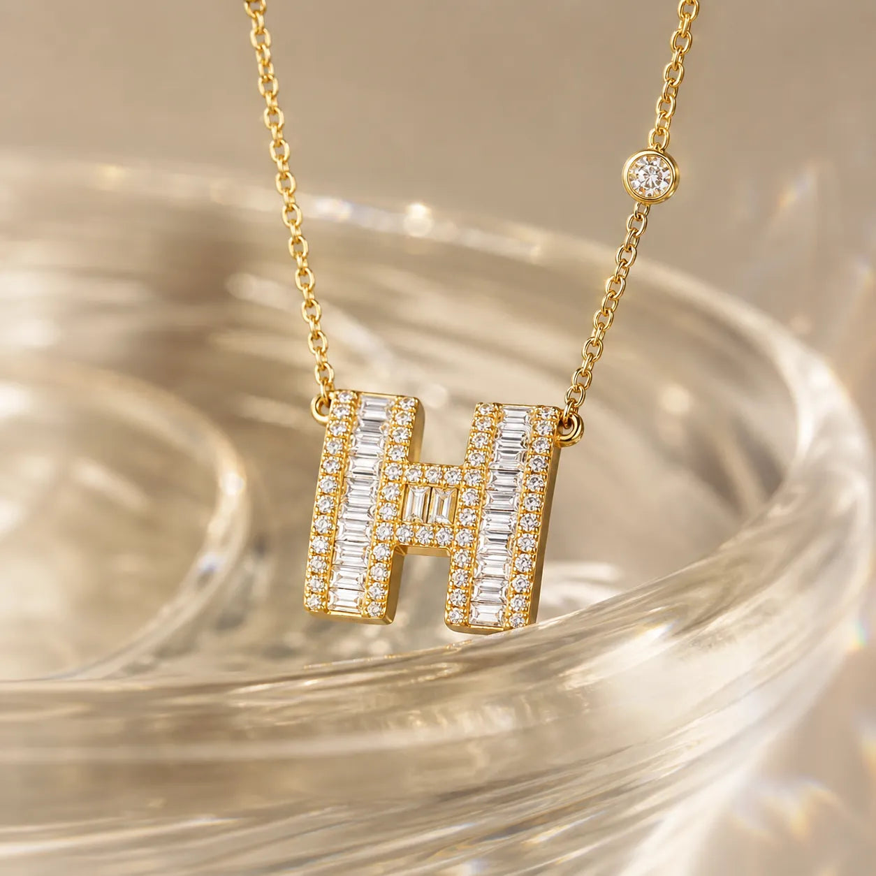 MUHUANG gold "H" pendant necklace with diamonds placed on a transparent surface, emphasizing shimmer and elegant design.