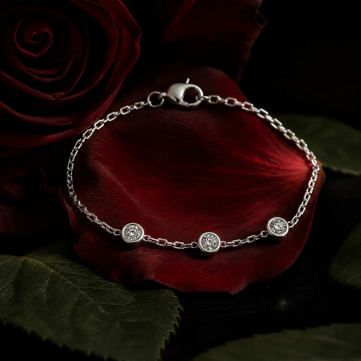 White gold bracelet with three round diamonds displayed on dark red rose petals, luxury jewelry presentation